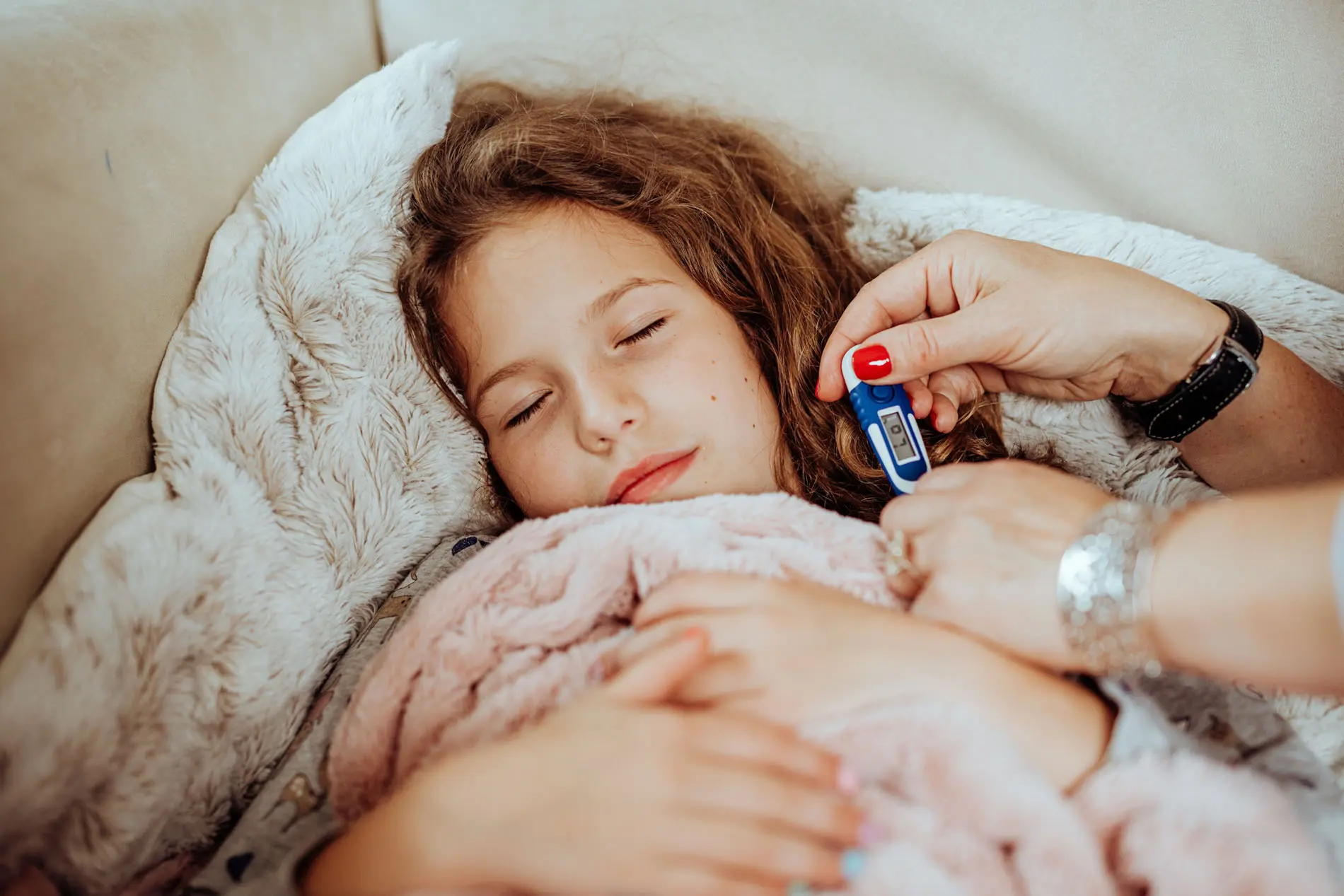Kind mit Erkältung auf Sofa in Decke gewickelt
